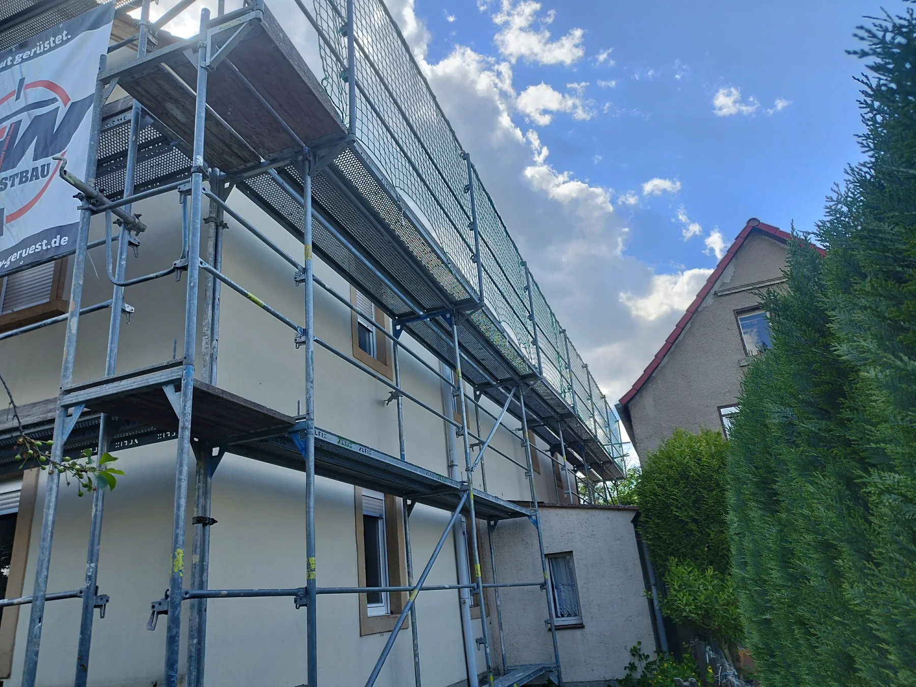 Fertig aufgebautes Dachdeckergerüst mit deutlich sichtbarem Dachfangnetz und SW-Gerüstbau-Plane